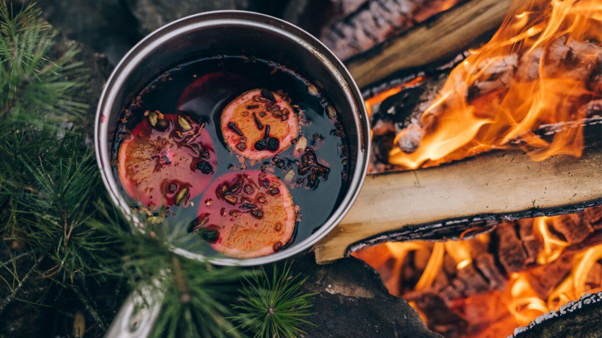 Ein Top mit Glühwein steht über einem Lagerfeuer.