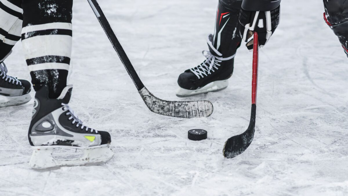 Zwei Eishockeyspieler aus dem Eis, die um den Puck kämpfen. Man sieht nur die Schlittschuhe, den Puck und die Schläger.