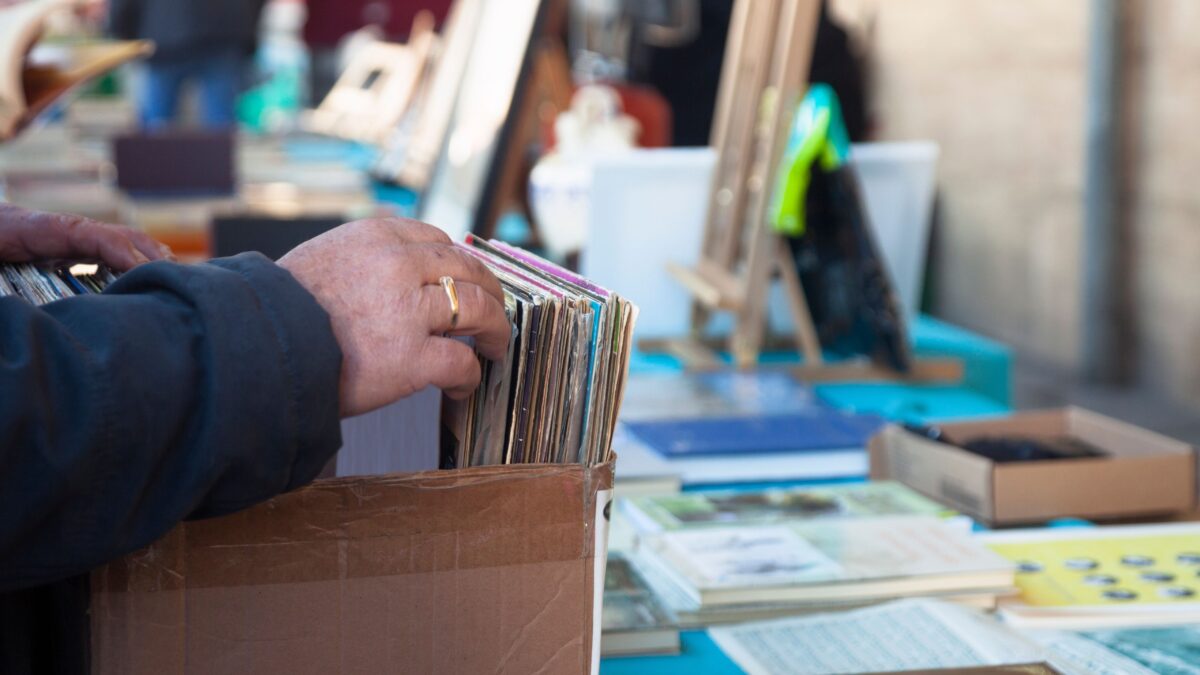 Eine Hand durchsucht einen Karton mit Comics, im Hintergrund liegen weitere Trödelsachen