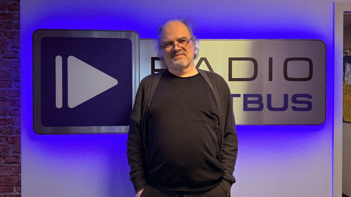 Autor und Regisseur Dominik Wilgenbus vor dem Radio Cottbus Logo