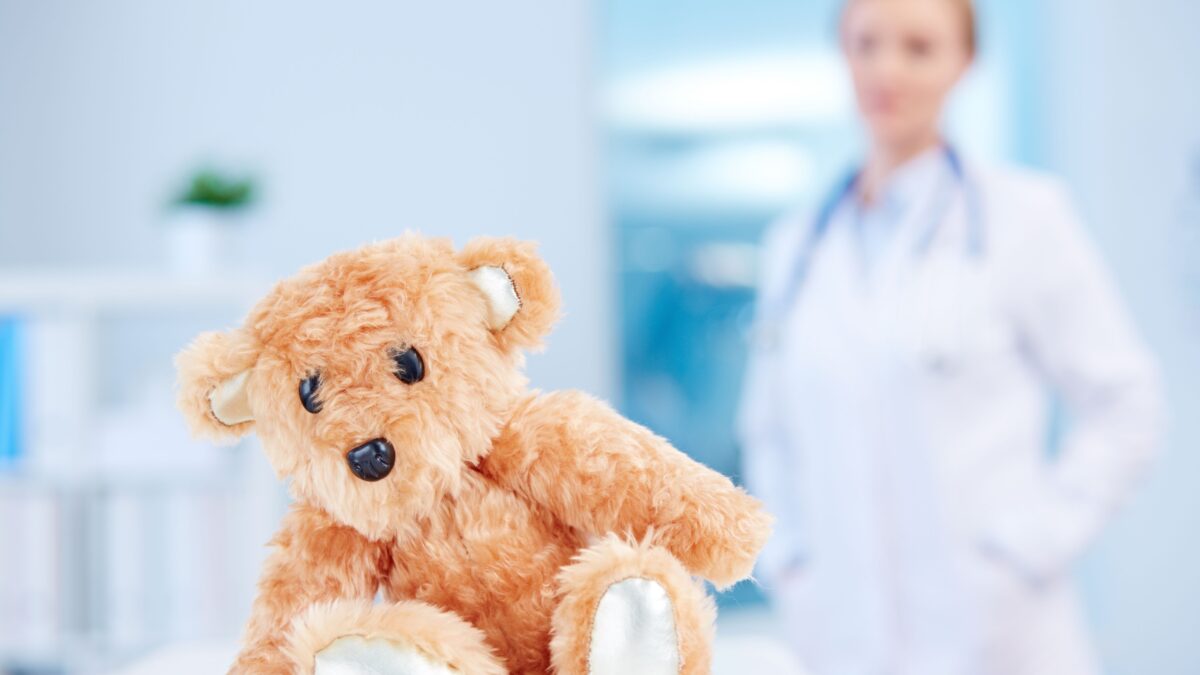 Im Hintergrund eine unscharfe Ärztin und im Vordergrund ein Teddybär